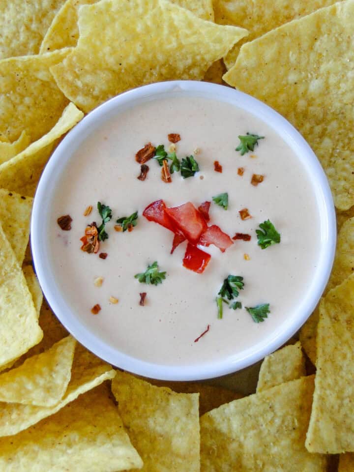 Close up top view of homemade queso dip in serving bowl garnished with extra tomatoes.