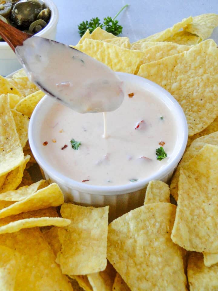 Spoonful of homemade queso dip drizzling off into serving bowl.