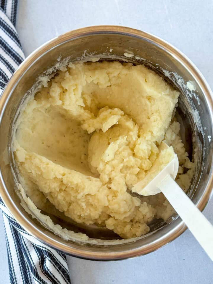 All ingredient stirred into mashed potatoes in instant pot with white spatula.