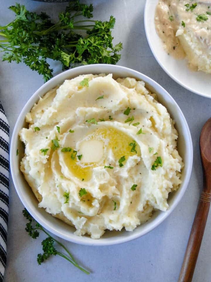 Top view of instant pot mashed potatoes in white round serving bowl with serving spoon to the side of bowl.