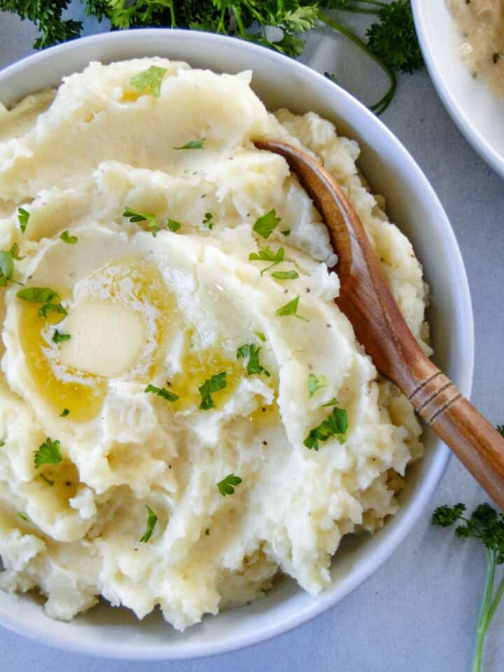 Top view of instant pot mashed potatoes in white serving bowl with wooden serving spoon in bowl.