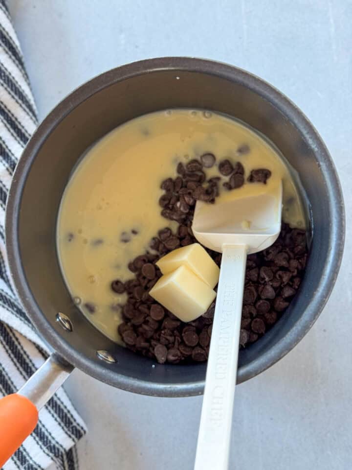 Sweetened condensed milk, chocolate chips and butter added to pot with white spatula.