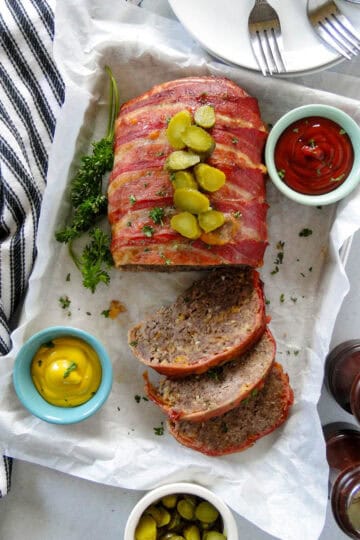 Top view of bacon cheeseburger meatloaf with slices cut off and topped with chopped pickles.