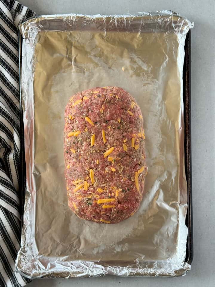 Meat mixture formed into loaf on aluminum foiled sheet pan.