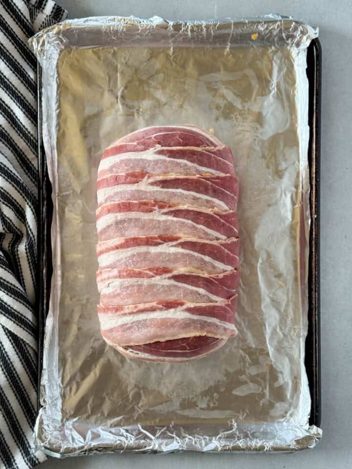Bacon wrapped around meatloaf on sheet pan.