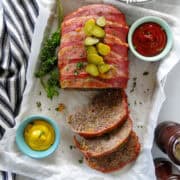 Top view of bacon cheeseburger meatloaf with slices cut off and topped with chopped pickles.