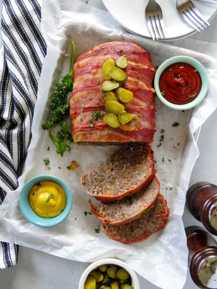 Top view of bacon cheeseburger meatloaf with slices cut off and topped with chopped pickles. 