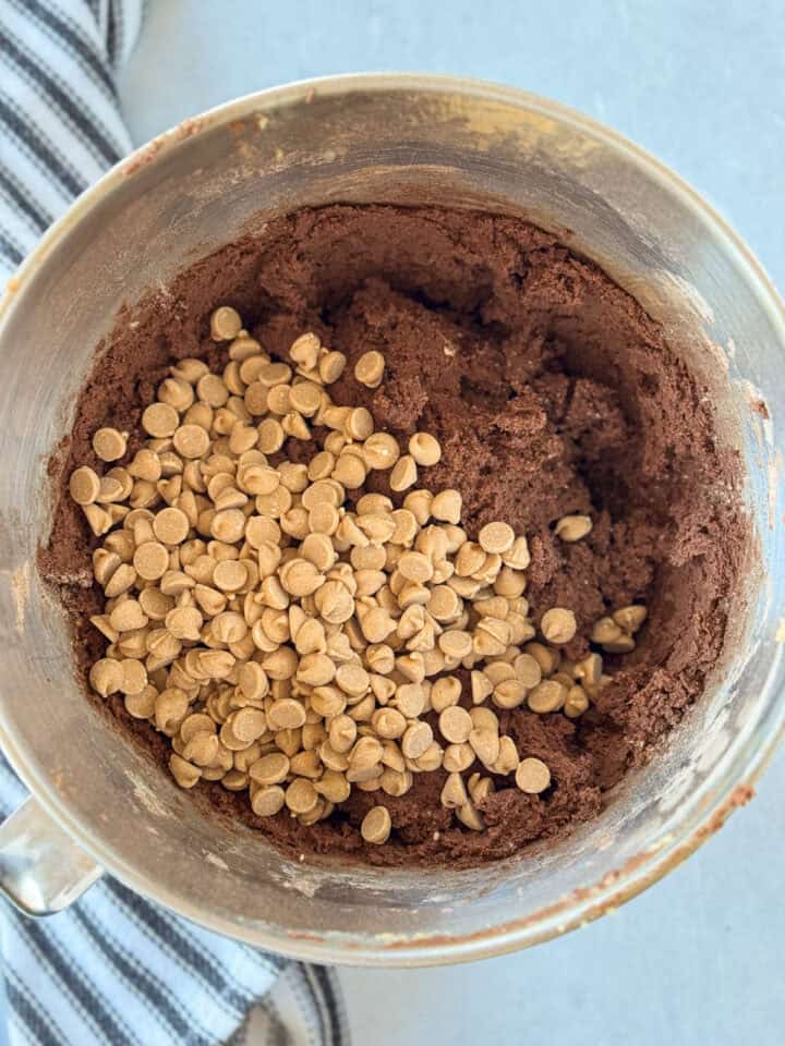 Peanut butter chips added to dough in metal mixing bowl.