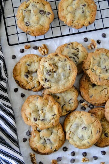 Top view of jumbo chocolate chip cookies in a pile in front of cooling rack of more cookies.