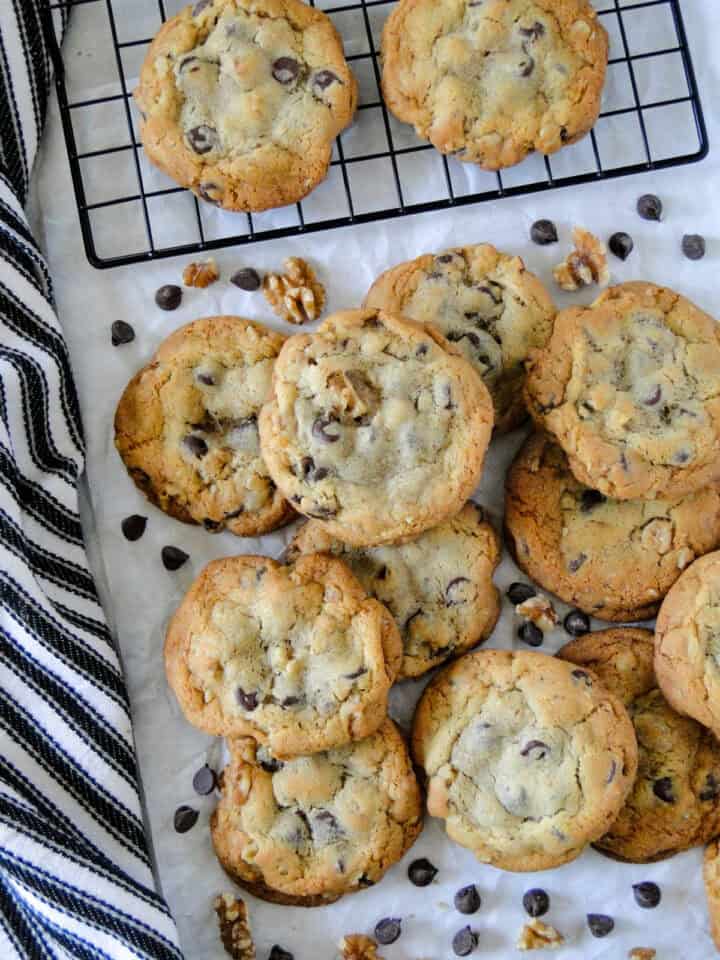 Top view of jumbo chocolate chip cookies in a pile in front of cooling rack of more cookies.