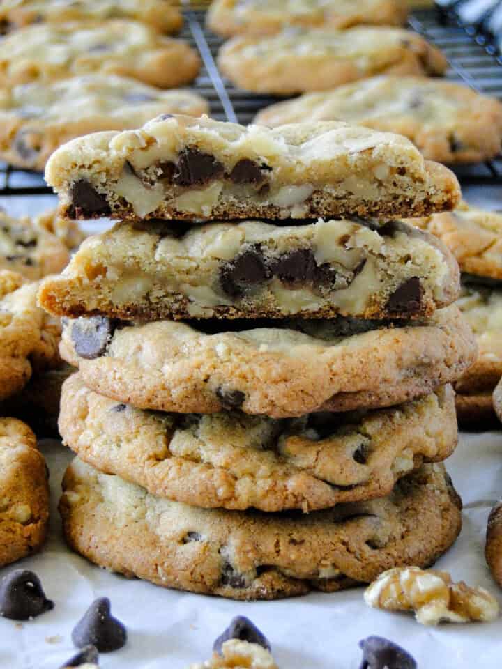 Chocolate chip walnut cookies stacked with top cookie cut in half showing chewy center.