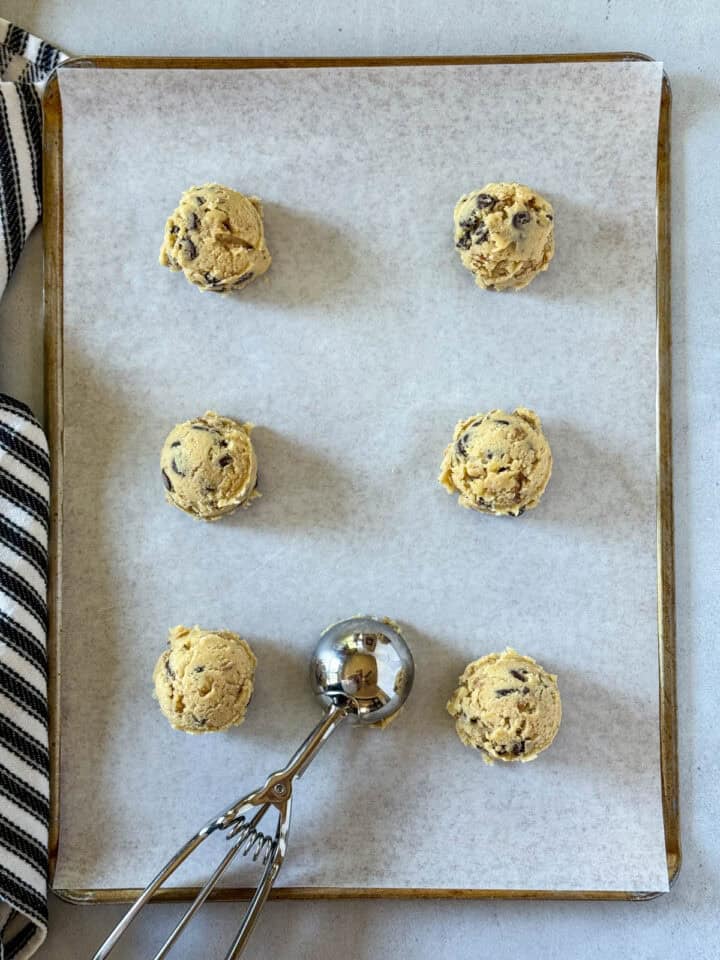 Cookie dough scoops on parchment lined cookie sheet with large scoop in the middle.