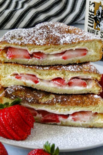 Close up side view of strawberries and cream stuffed french toast cut in half and stacked showing centers on white round plate.