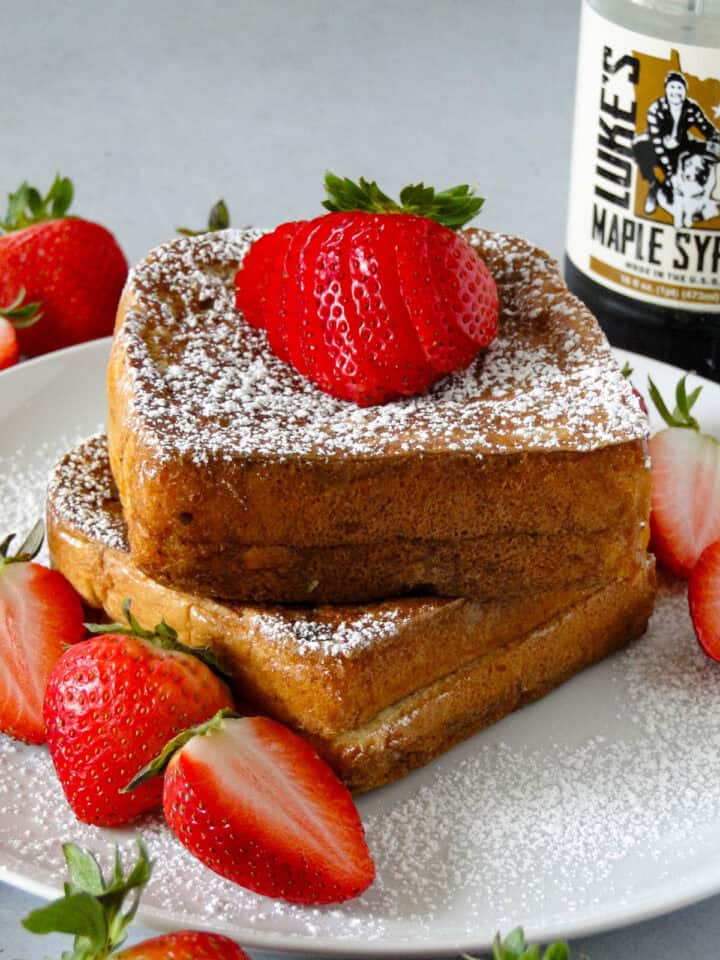 Two servings of stuffed french toast stacked on white round plate and garnished with powdered sugar and strawberries.