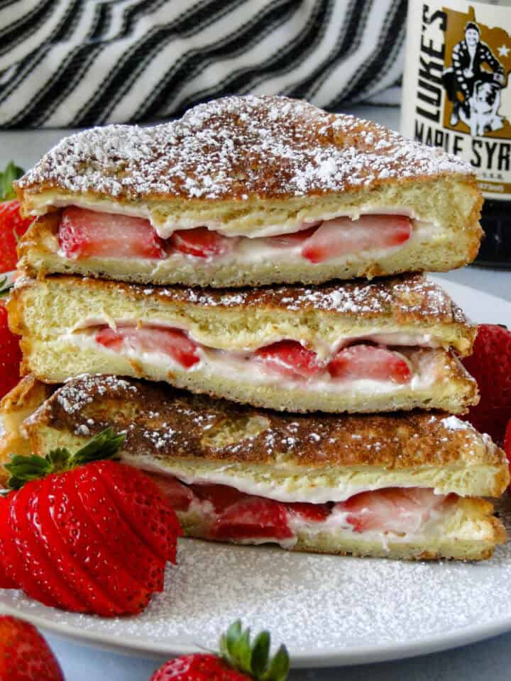 Close up side view of strawberries and cream stuffed french toast cut in half and stacked showing centers on white round plate.