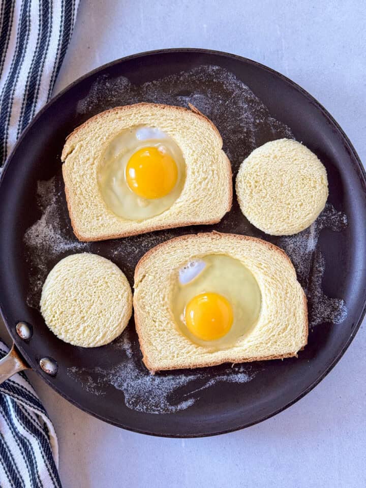 Eggs added to center holes of bread on skillet.