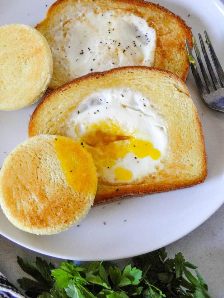 Close up view of egg in a hole on a plate with center piece of bread dipped in egg with yolk on it.