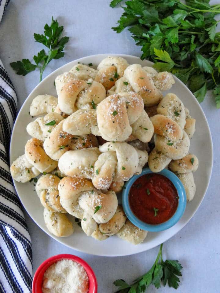 Homemade garlic knots on a plate with marinara dipping sauce on the side.