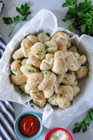 Homemade garlic knots in basket lined with parchment paper.