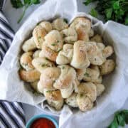 Homemade garlic knots in basket lined with parchment paper.