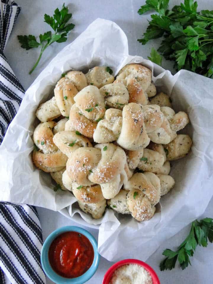 Homemade garlic knots in basket lined with parchment paper. 