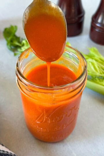 Homemade buffalo sauce drizzling off of a spoon into a mason jar.